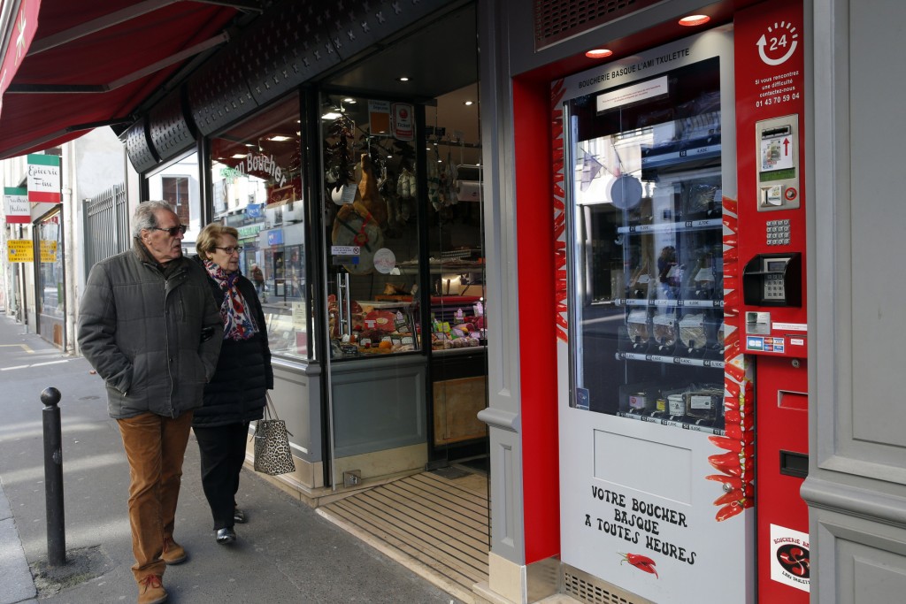 Residents watch the first meat vending machine installed in the French capital, in Paris, Tuesday, March 15, 2016. With their beloved baguette already available 24 hours a day, it seems only logical that Parisians can now get the Bayonne ham and Basque pate that goes so well with it from the first meat vending machine installed in the French capital. (AP Photo/Christophe Ena)