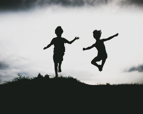 Silhouettes of kids jumping from a sand cliff at the beach. Active healthy kids enjoying their time at the beach. Fraternal twins playing together. Friends having fun during summer vacation. Nice day at the lake.