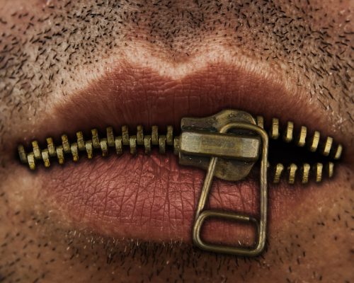 Close up of man's mouth with bronze or gold metal zipper closing lips shut.