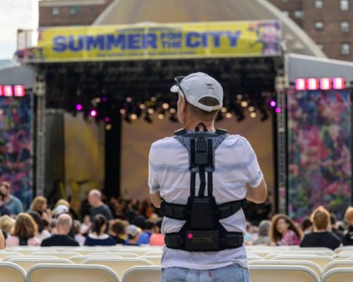 A concertgoer wears haptic suits created for the deaf by Music: Not Impossible, during an outdoor concert at Lincoln Center on July 22, 2023, in New York City. - The violins reverberate in the ribcage, while cello and bass are felt a little further down, with horns in the shoulders, and more often than not, soloists in the wrists. That's one way audio expert Patrick Hanlon programs wireless haptic suits designed to enable the deaf or hard of hearing to experience orchestral music, as initiatives to improve inclusivity at live music performances break new ground. At the Lincoln Center concert, audience members tried vests featuring 24 points of vibration that translate the music onstage. (Photo by ANGELA WEISS / AFP)