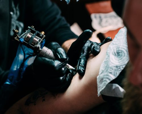 cropped shot of tattooing process of tattoo on shoulder in salon